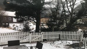 Et sneklædt udendørsområde med hvidt plankeværk, et bord med stole og en bænk.