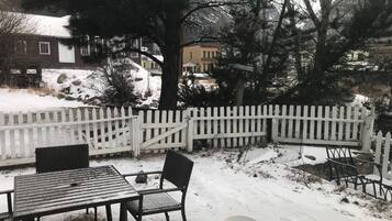 Een besneeuwde buitenplaats met een witte picket fence, een tafel met stoelen en een bank.
