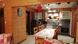 A cozy kitchen with wooden walls, a dining table with chairs, and a red heart decoration. - Charming 4* chalet with panoramic view, south-facing, sleeps 6. (Gérardmer)