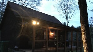 A wooden cabin with a porch, a trash can, and a clear sky. - Reid's Hidden River Getaway (Luther)