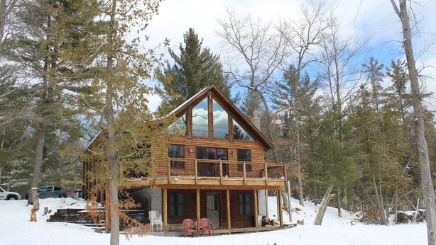 A wooden cabin with a balcony, surrounded by trees and snow. - Reid's Hidden River Getaway (Luther)