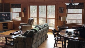 A spacious living room with a wooden floor, a sofa, a television, and a dining area with a table and chairs. - Reid's Hidden River Getaway (Luther)