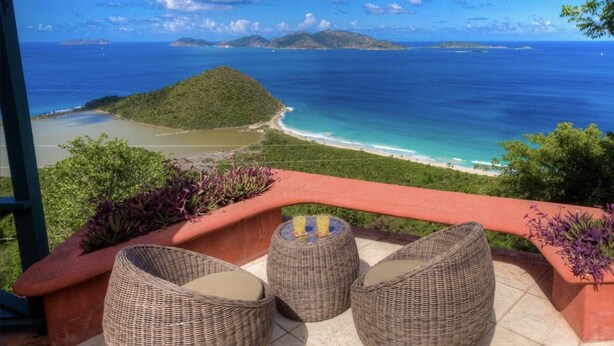 A balcony with wicker chairs and a view of a beach and ocean.
