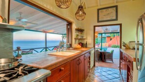 A kitchen with a view of the sea, a dining area with outdoor seating, and a ceiling fan.