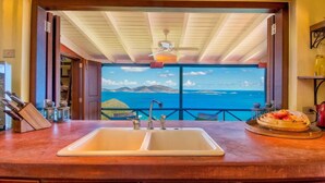 A kitchen with a double sink, a ceiling fan, and a view of the ocean.