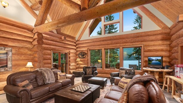 A log cabin interior with a fireplace, leather furniture, and large windows offering views of the outdoors. - Lake front Lodge on Lake Swift (Cougar)