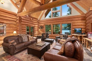 A log cabin interior with a fireplace, leather furniture, and large windows offering views of the outdoors. - Lake front Lodge on Lake Swift (Cougar)