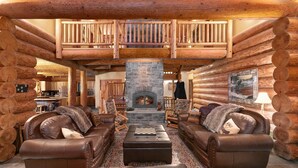 A log cabin interior with a stone fireplace, leather sofas, and a wooden staircase. - Lake front Lodge on Lake Swift (Cougar)