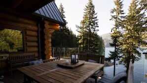 A wooden deck with a table and benches overlooking a lake, surrounded by trees. - Lake front Lodge on Lake Swift (Cougar)