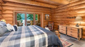 A log cabin bedroom with a large bed, a dresser, a chair, and a view of the outdoors. - Lake front Lodge on Lake Swift (Cougar)