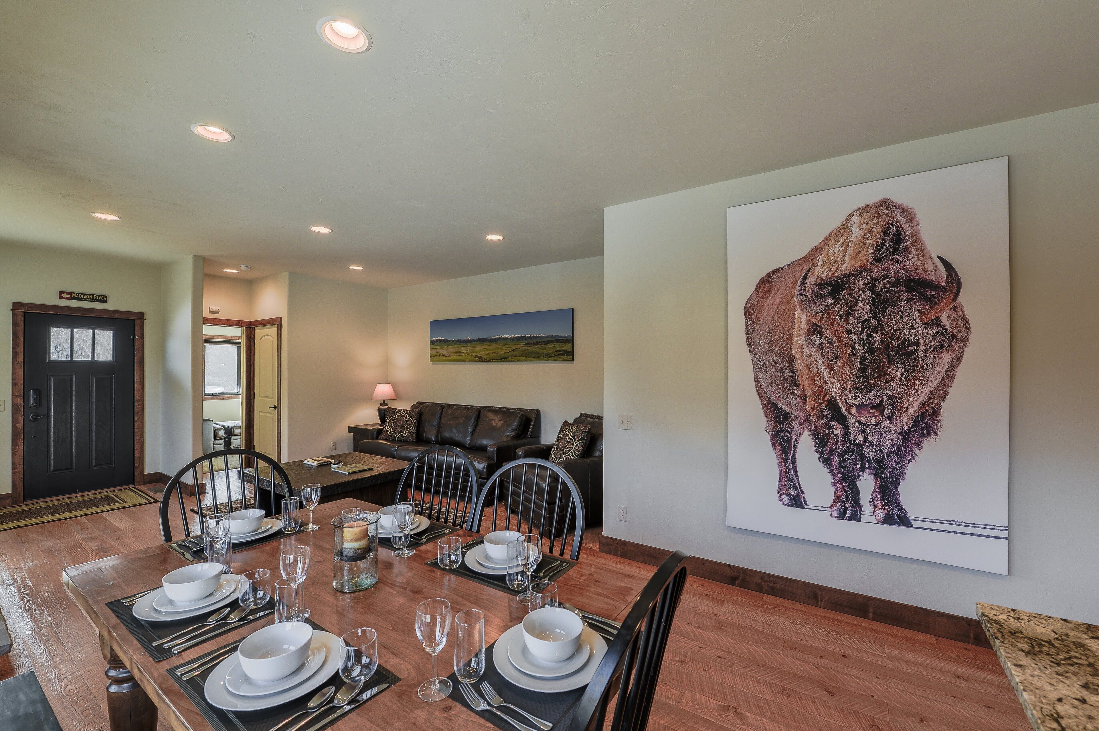 A dining area with a wooden table set for four, a large buffalo painting on the wall, and a dark door labeled "Madison Street".