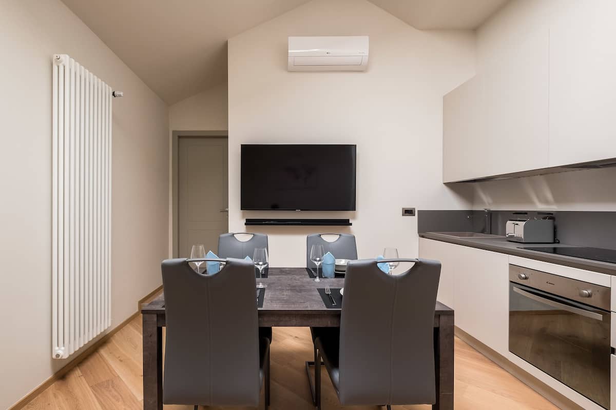 Een moderne keuken met een eethoek, voorzien van een grote flatscreen-tv, een inbouwoven en een eettafel met stoelen.