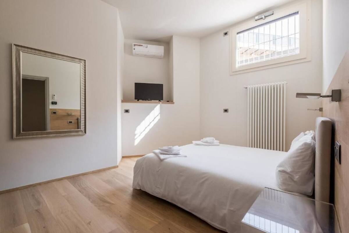 Een slaapkamer met een bed, een spiegel, een televisie en een raam.