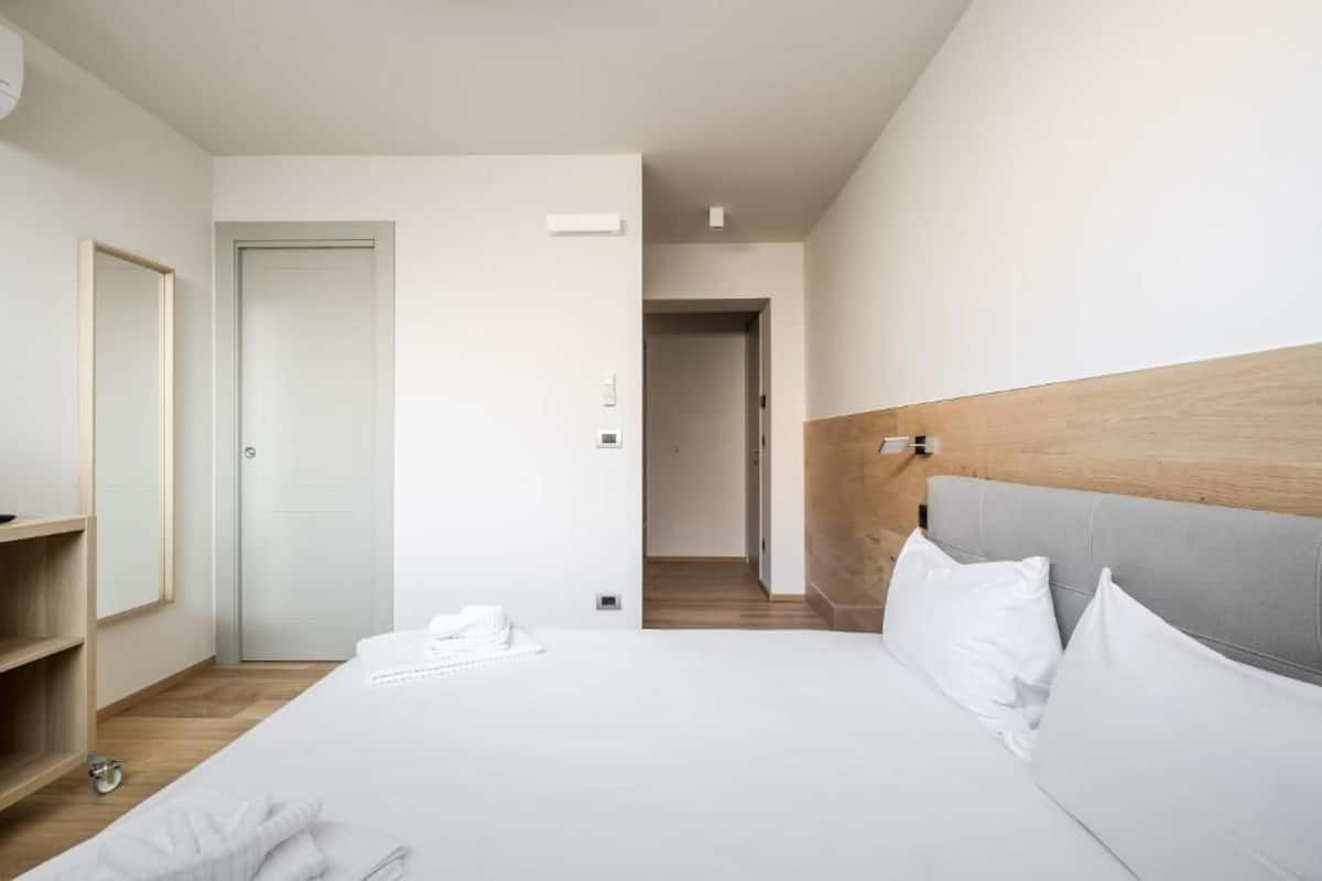 Een hotelkamer met een groot bed, een houten hoofdbord, een spiegel en een deur naar een andere kamer.