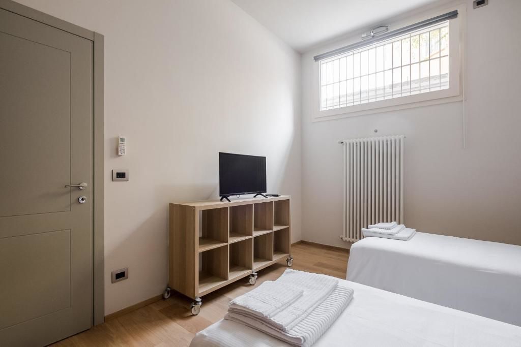 Ein Hotelzimmer mit Bett, Fernseher auf einem Holzboden, Heizkörper und einem Fenster mit Jalousien.