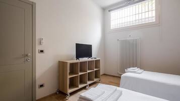 Ein Hotelzimmer mit Bett, Fernseher auf einem Holzboden, Heizkörper und einem Fenster mit Jalousien.
