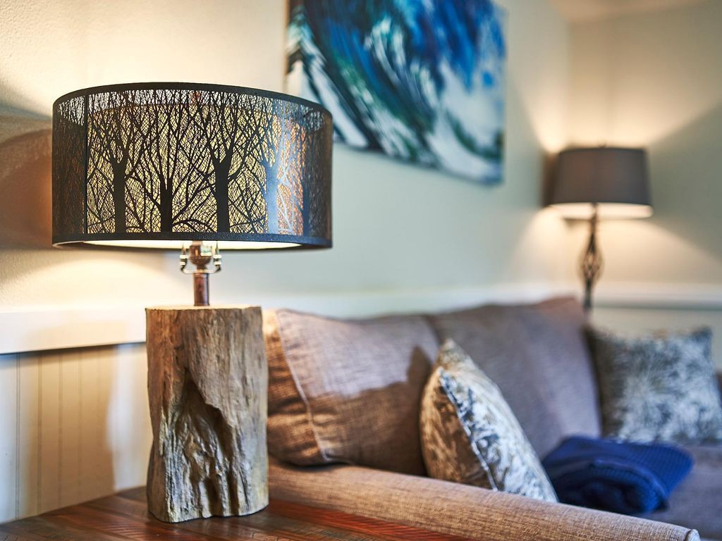 A lamp with a tree design on a wooden stand, a sofa with cushions, and a painting on the wall.