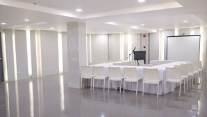 Een vergaderzaal met een lange tafel, witte stoelen, een spreekgestalte en een projectiescherm.