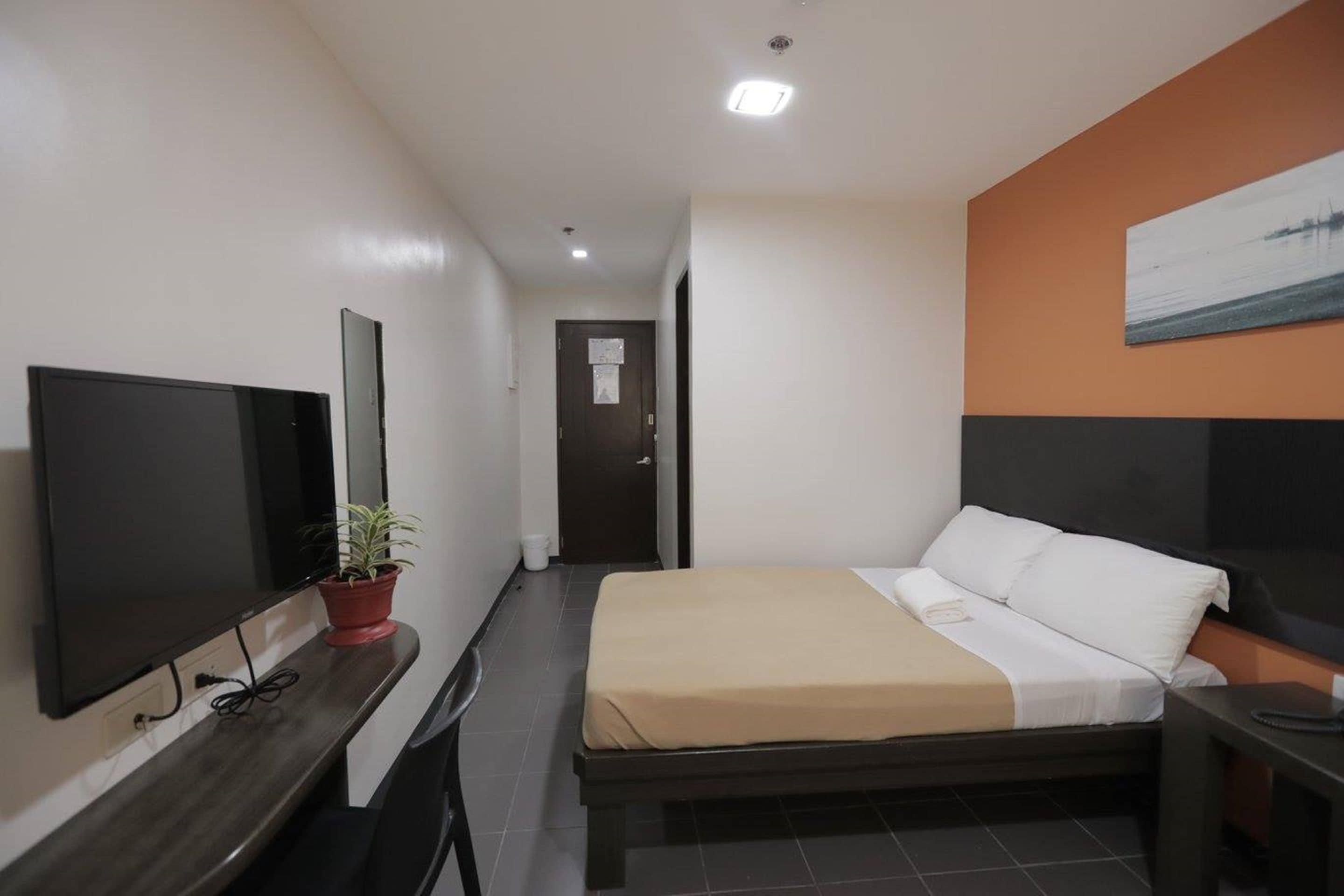 Une chambre d’hôtel avec un lit, une télévision, un bureau et une plante en pot.
