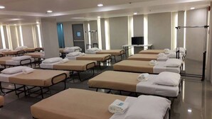 Een hotelkamer met meerdere bedden, elk met een witte deken en kussen, in rijen gerangschikt.