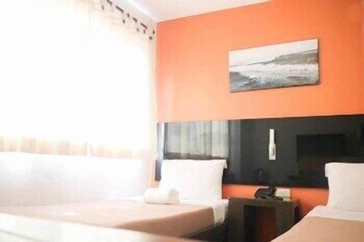 A hotel room with a bed, a bedside table, a TV, and a painting on the wall.