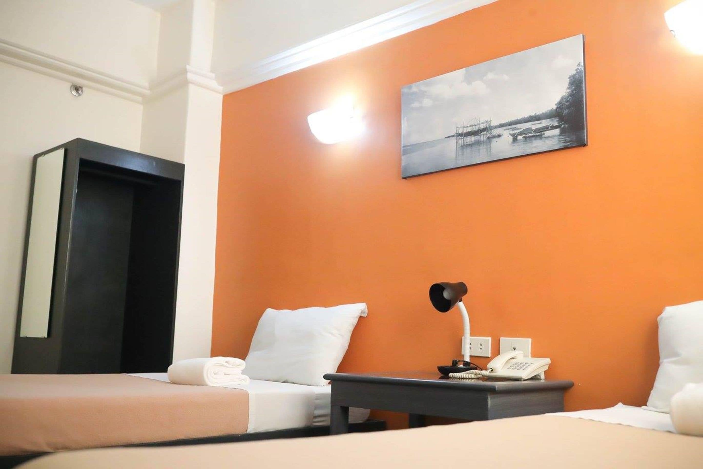Quarto de hotel com duas camas, uma escrivaninha com abajur, telefone e um quadro na parede.