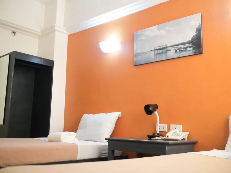 Quarto de hotel com duas camas, uma escrivaninha com abajur, telefone e um quadro na parede.