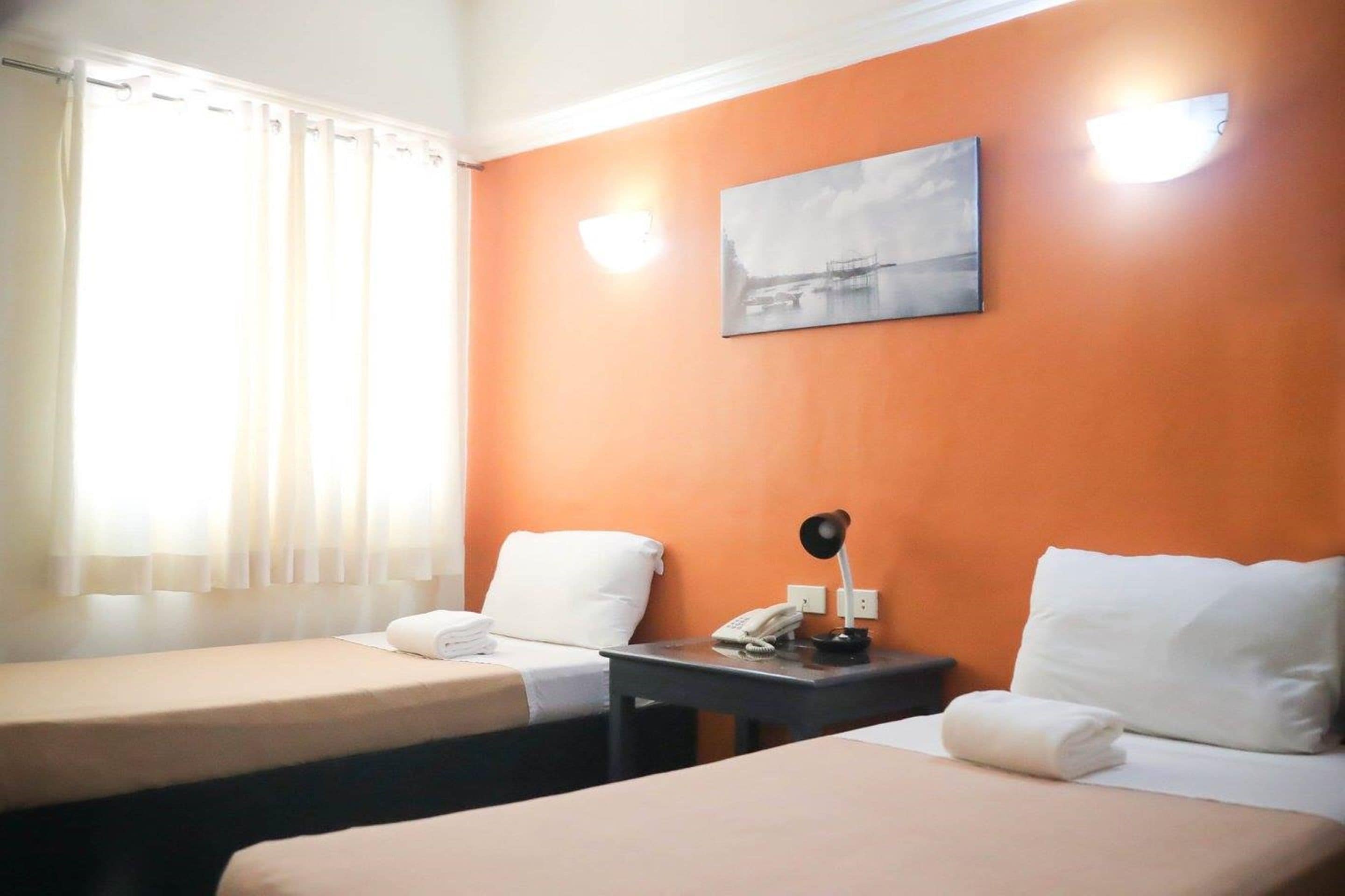 A hotel room with two beds, a nightstand with a phone, and a painting on the wall.