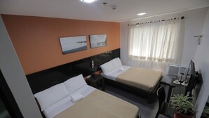 Een hotelkamer met twee bedden, een bureau, een stoel, een potplant en een raam met gordijnen.