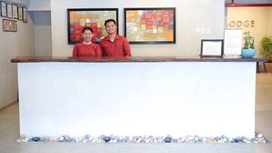Een receptiebalie met twee medewerkers, inlijstingen met certificaten aan de muur, en een bordje met de tekst 'LODGE'.
