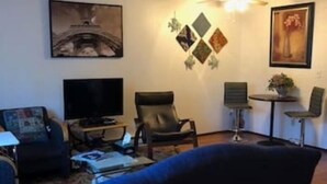 En stue med sofa, fjernsyn, stol og et lille bord med en plante.
