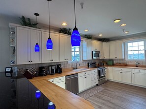 A modern kitchen with white cabinets, a wooden countertop, a built-in microwave, and pendant lights.