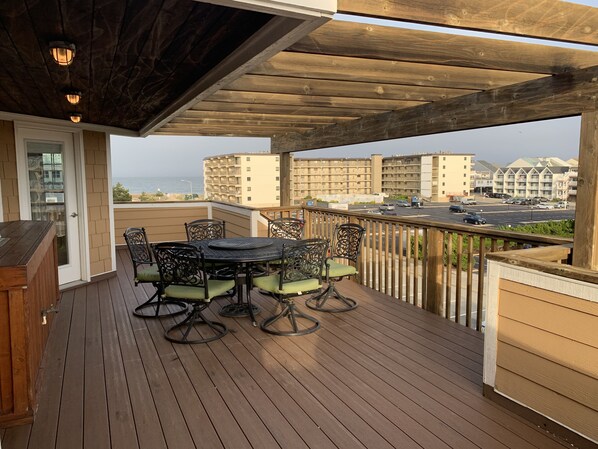 Una terraza de madera con una mesa y sillas, con vista a un paisaje urbano y al océano.