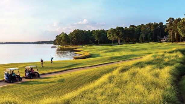 Um campo de golfe com um corpo de água, árvores e uma casa ao fundo.