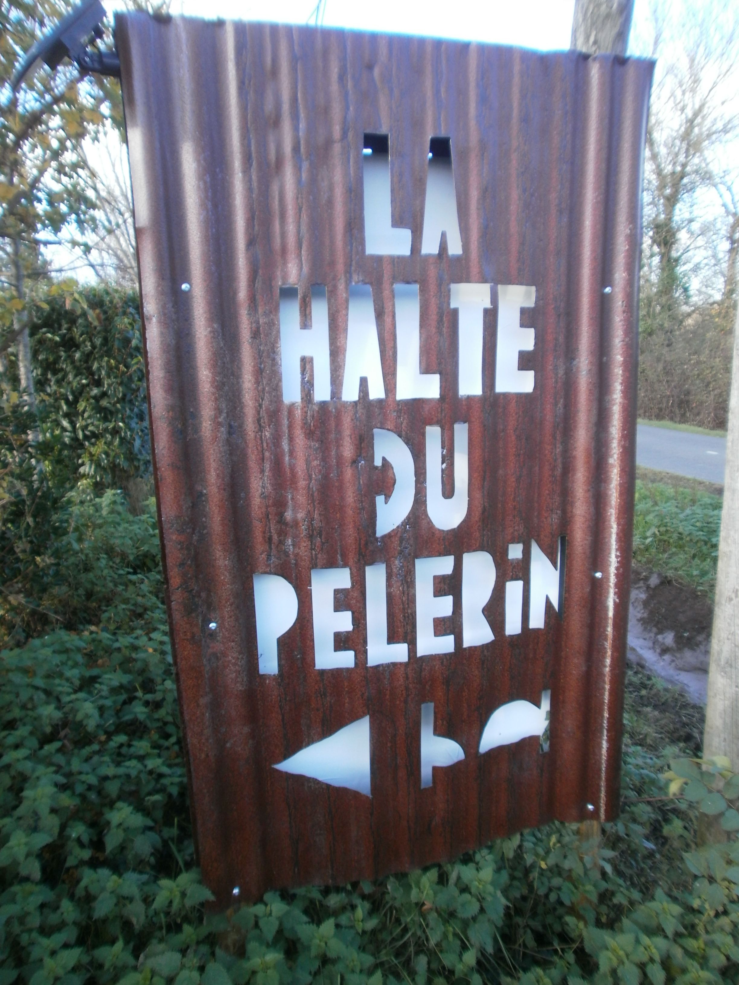 A rusted metal sign with the text "LA HALTE DU PELERIN" and directional arrows.