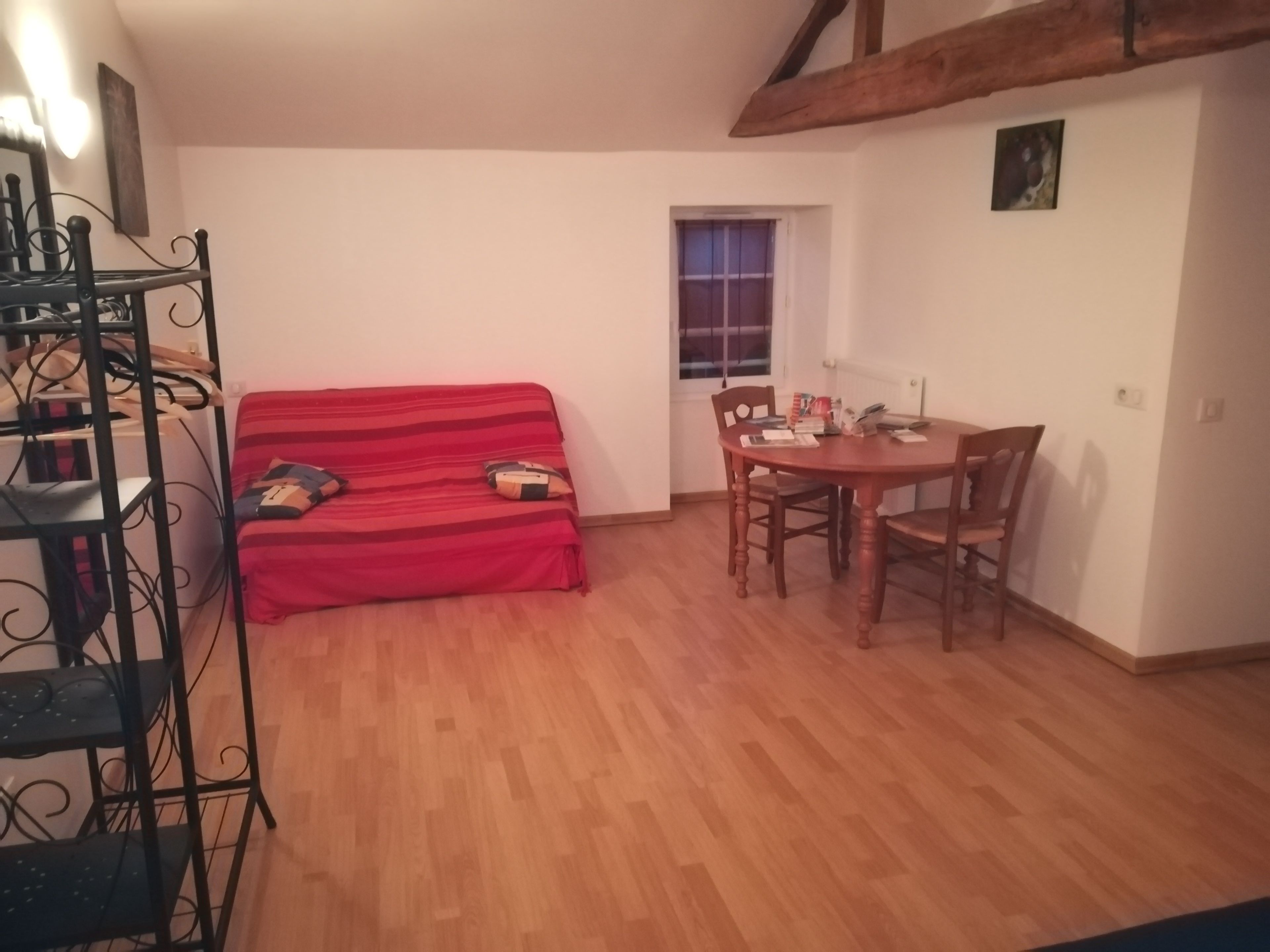 Una sala acogedora con un sofá rojo, una mesa de comedor de madera con sillas y una estantería de metal.