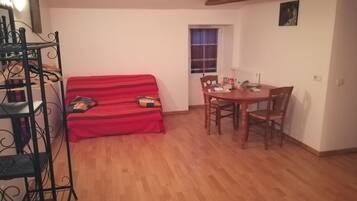 Una sala acogedora con un sofá rojo, una mesa de comedor de madera con sillas y una estantería de metal.
