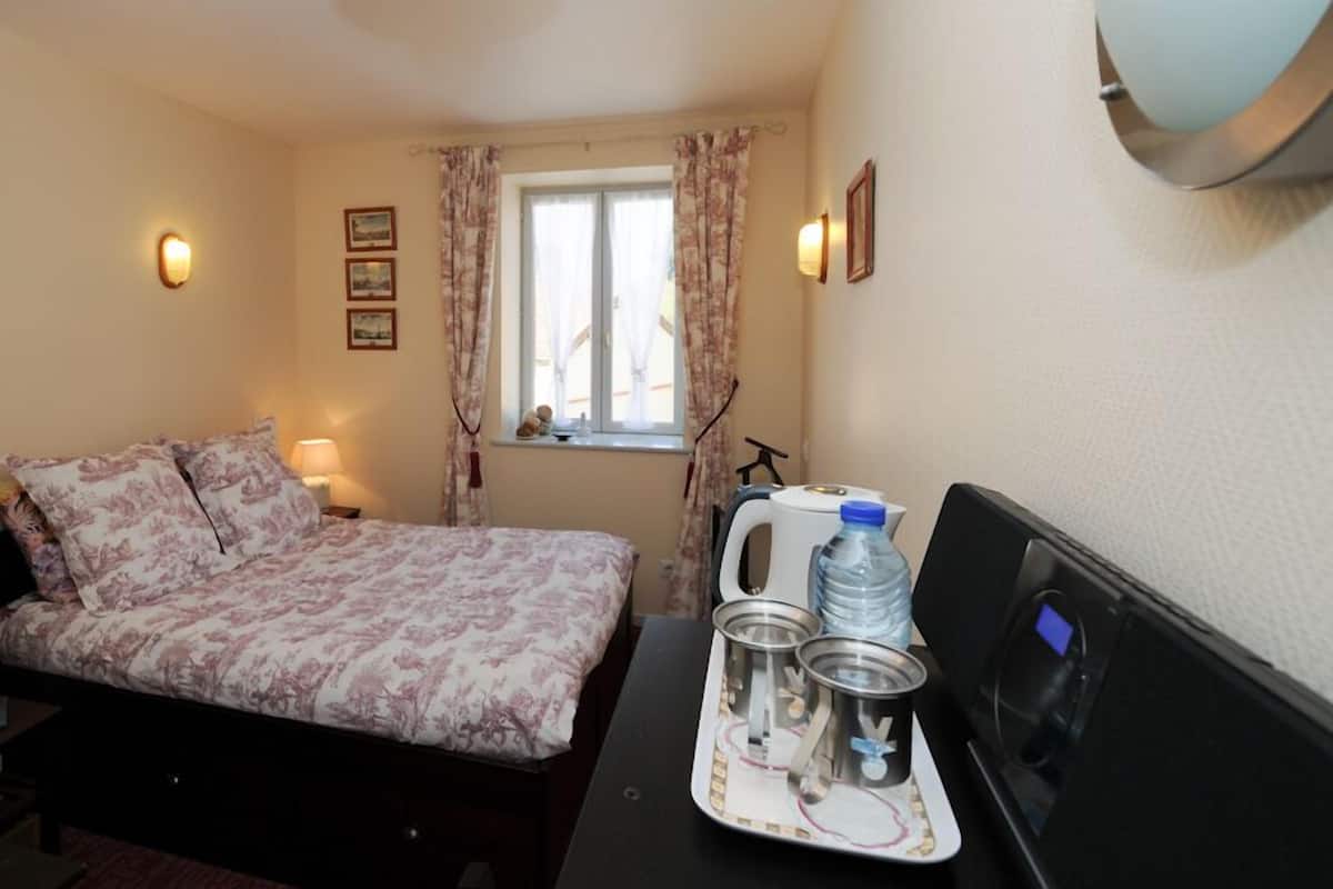 Habitación de hotel con cama, escritorio con objetos sobre una bandeja, ventana con cortinas e iluminación en la pared.