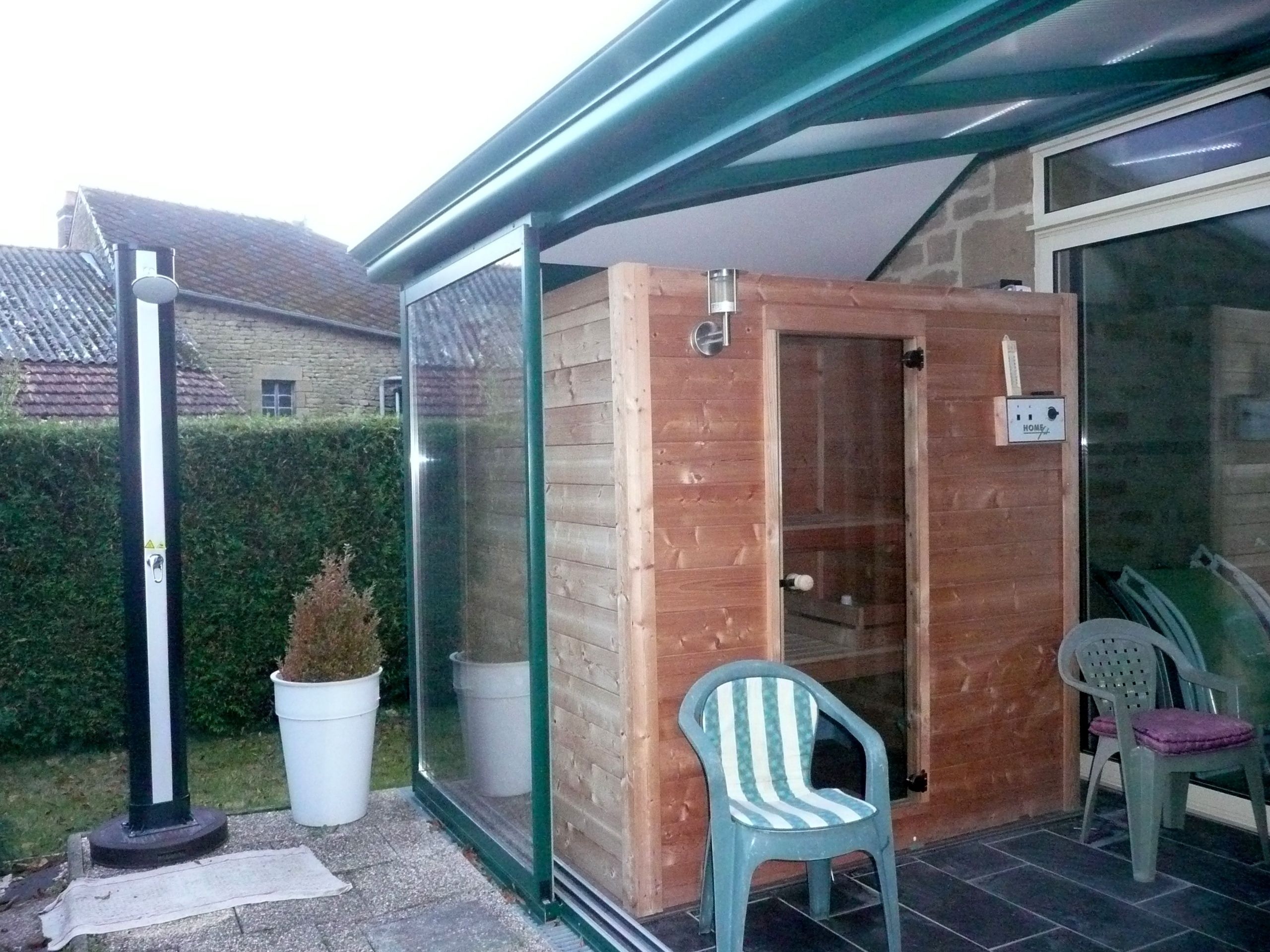 A wooden sauna structure with a glass door, a small chair, and a "HOME" sign on the wall.