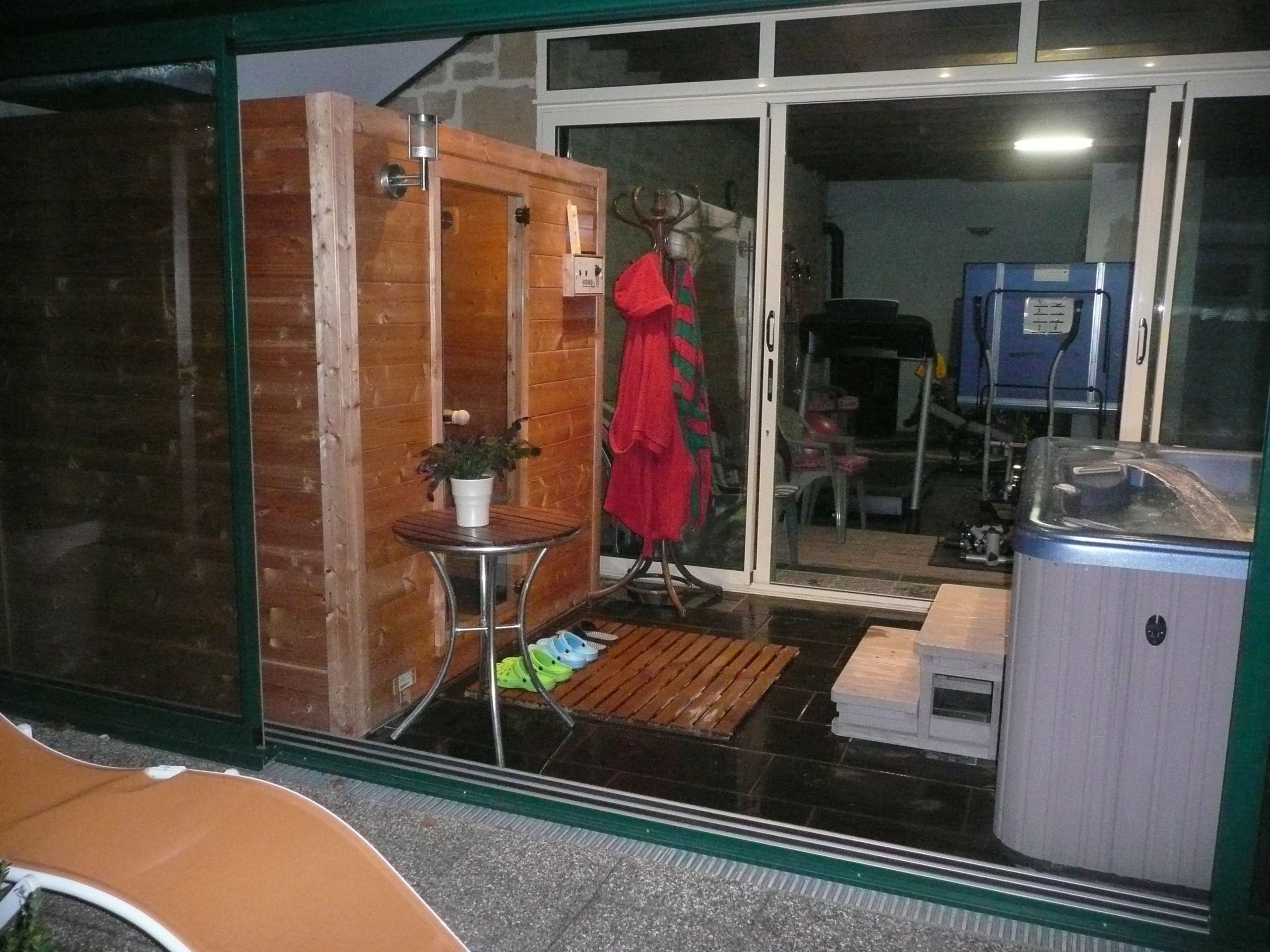 A room with a wooden door, a small table with a potted plant, a red coat on a chair, and a hot tub.