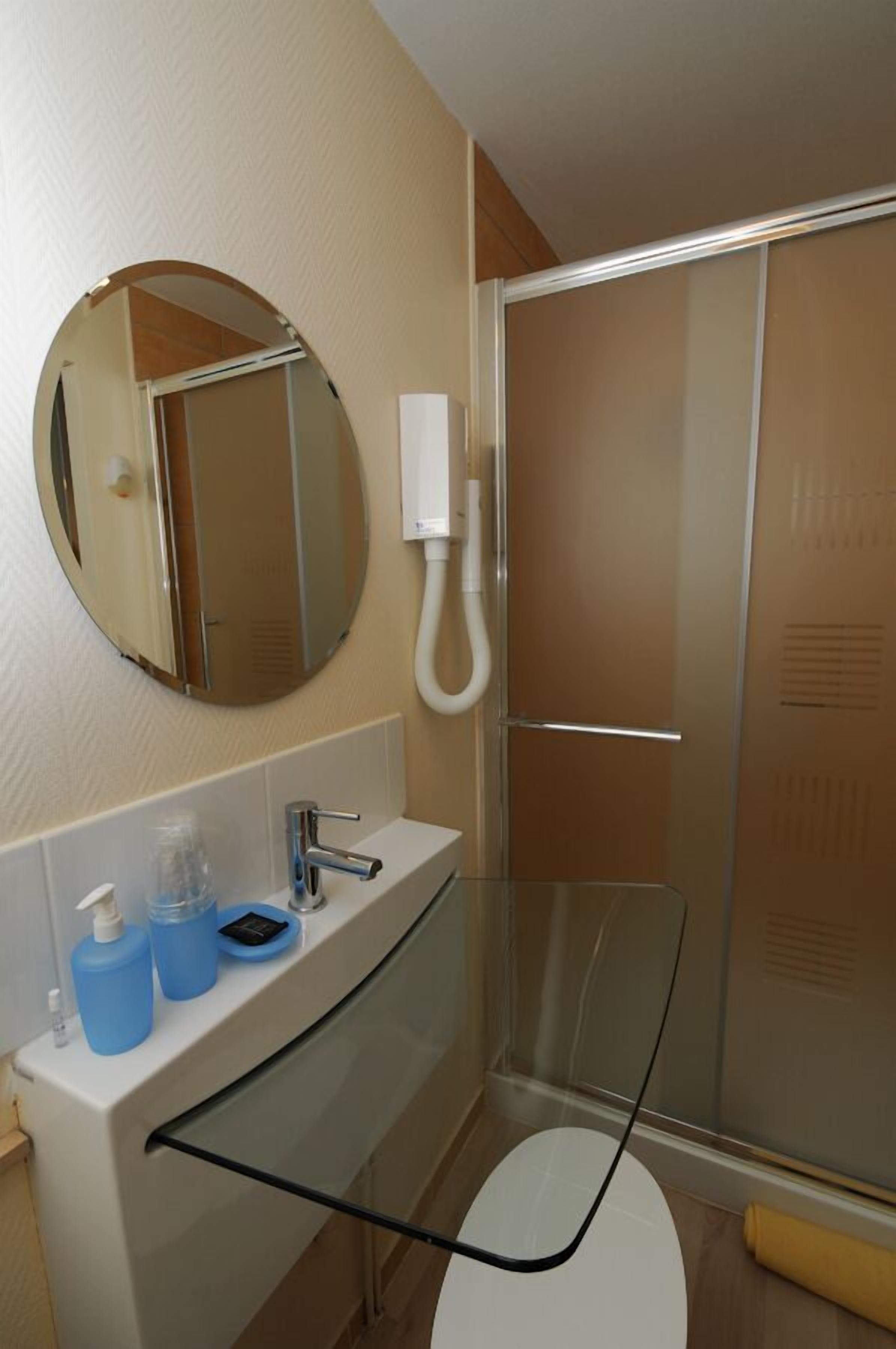 Un baño moderno con cabina de ducha de vidrio, un espejo redondo y un lavamanos blanco con dispensador de jabón.