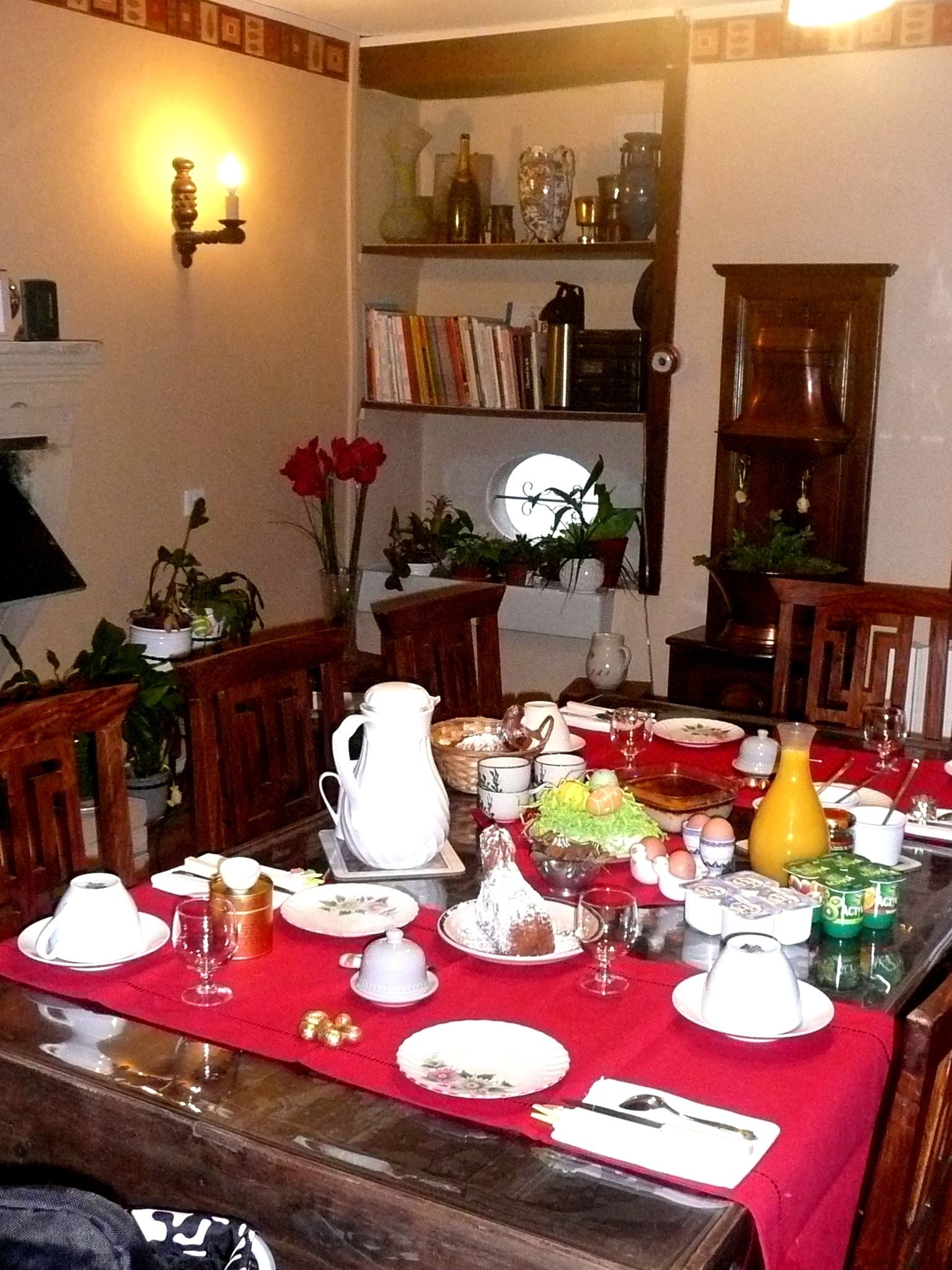 A dining room with a table set for a meal, surrounded by chairs, a bookshelf, and a fireplace.