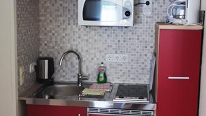 Een compacte keuken met rode kastjes, een magnetron, een koffiezetapparaat en een spoelbak.