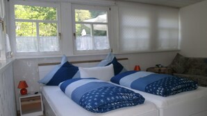 Een slaapkamer met een bed, twee ramen, een nachtkastje, een lamp en een bank.
