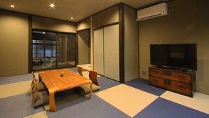 A room with a wooden table and chairs, a television on a dresser, and a sliding door leading to a balcony. - Chizuruan (Kyoto)