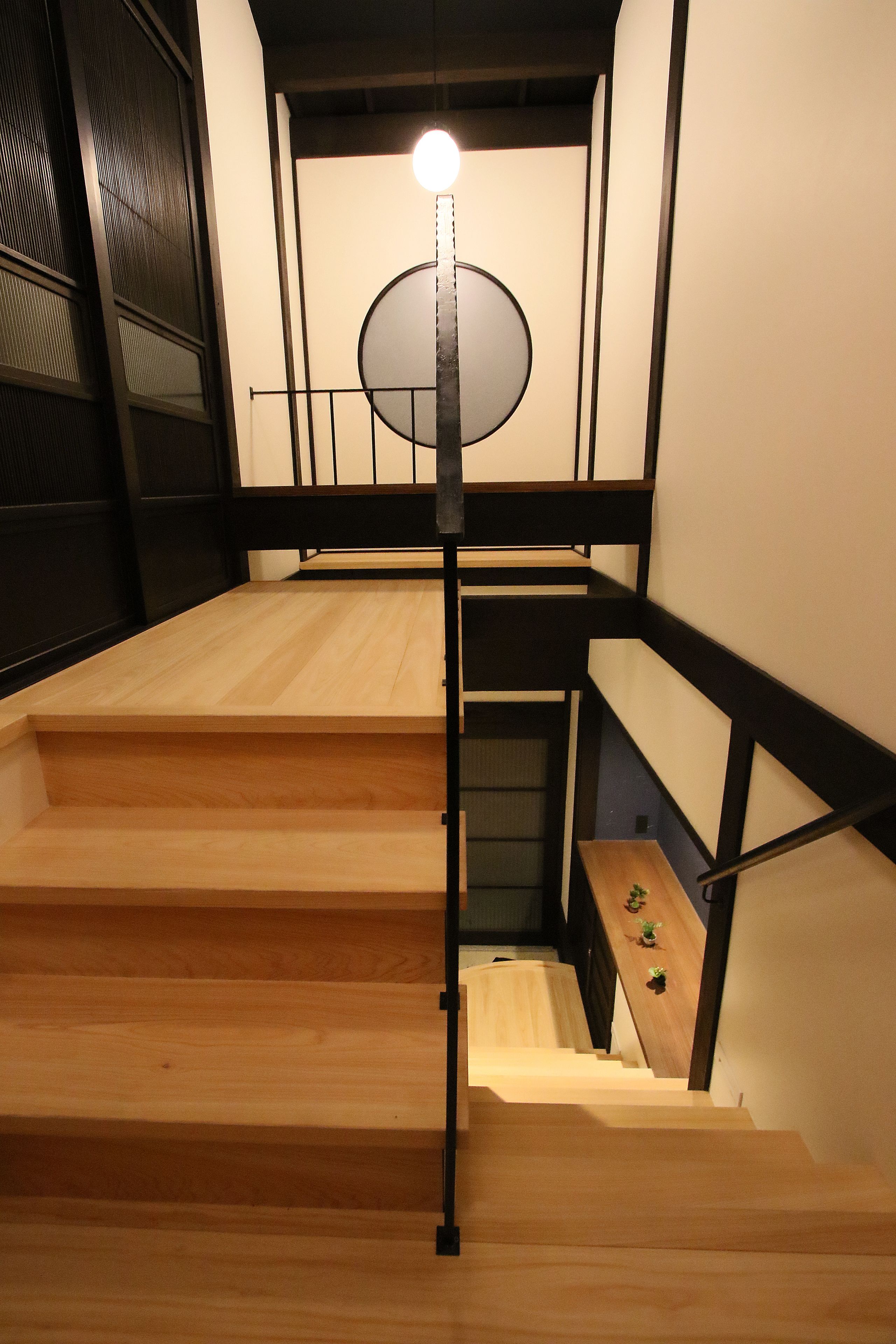 Un escalier en bois avec des rampes noires et un luminaire au sommet.