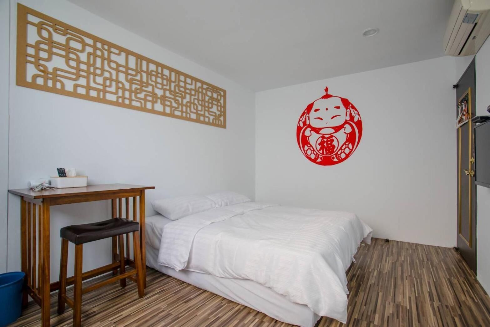 A room with a bed, a desk, a chair, a blue trash bin, and a decorative wall piece.
