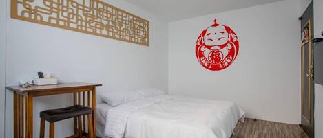 A room with a bed, a desk, a chair, a blue trash bin, and a decorative wall piece.