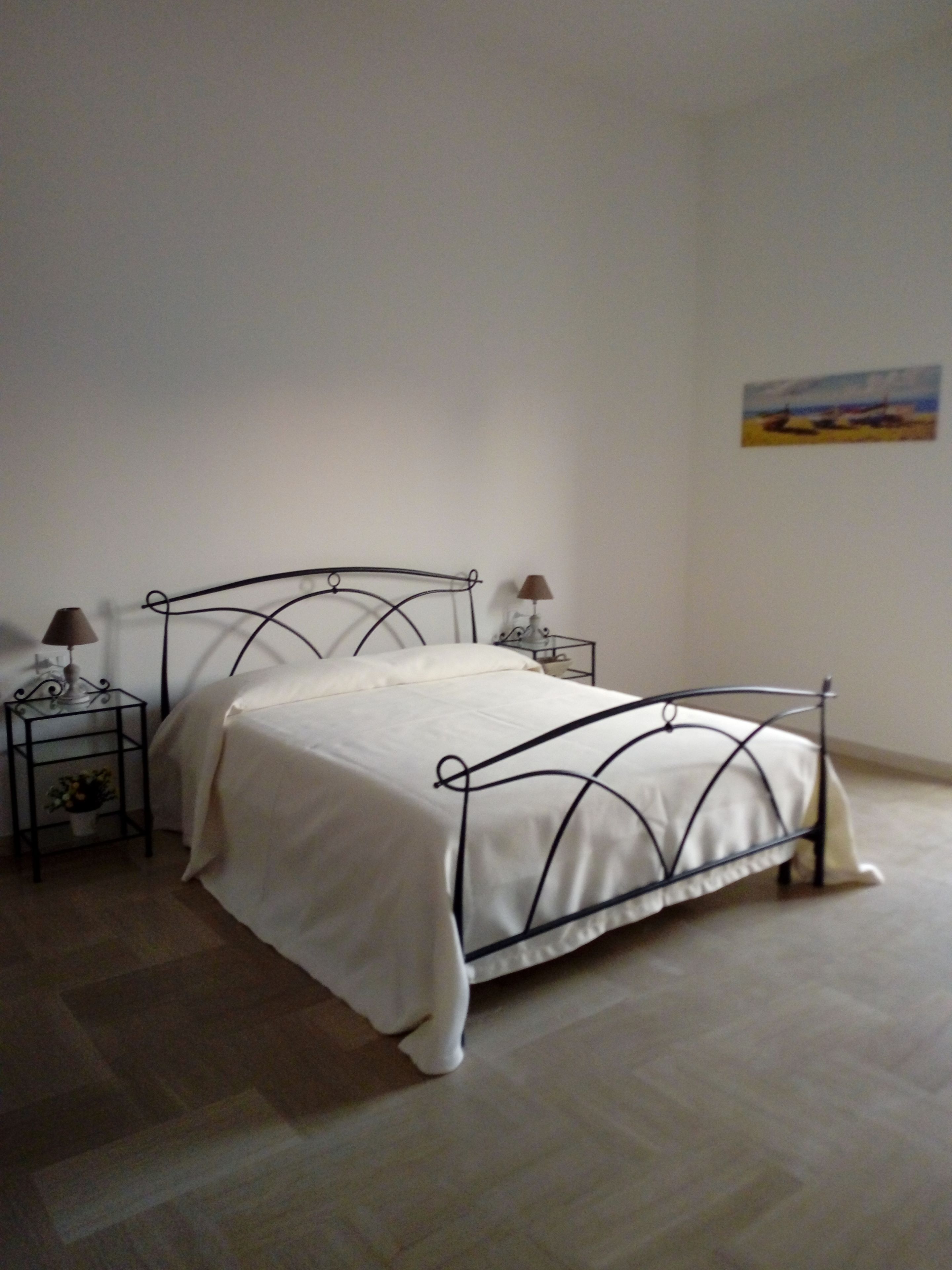 A bed with a metal frame and white bedding in a room with a tiled floor.