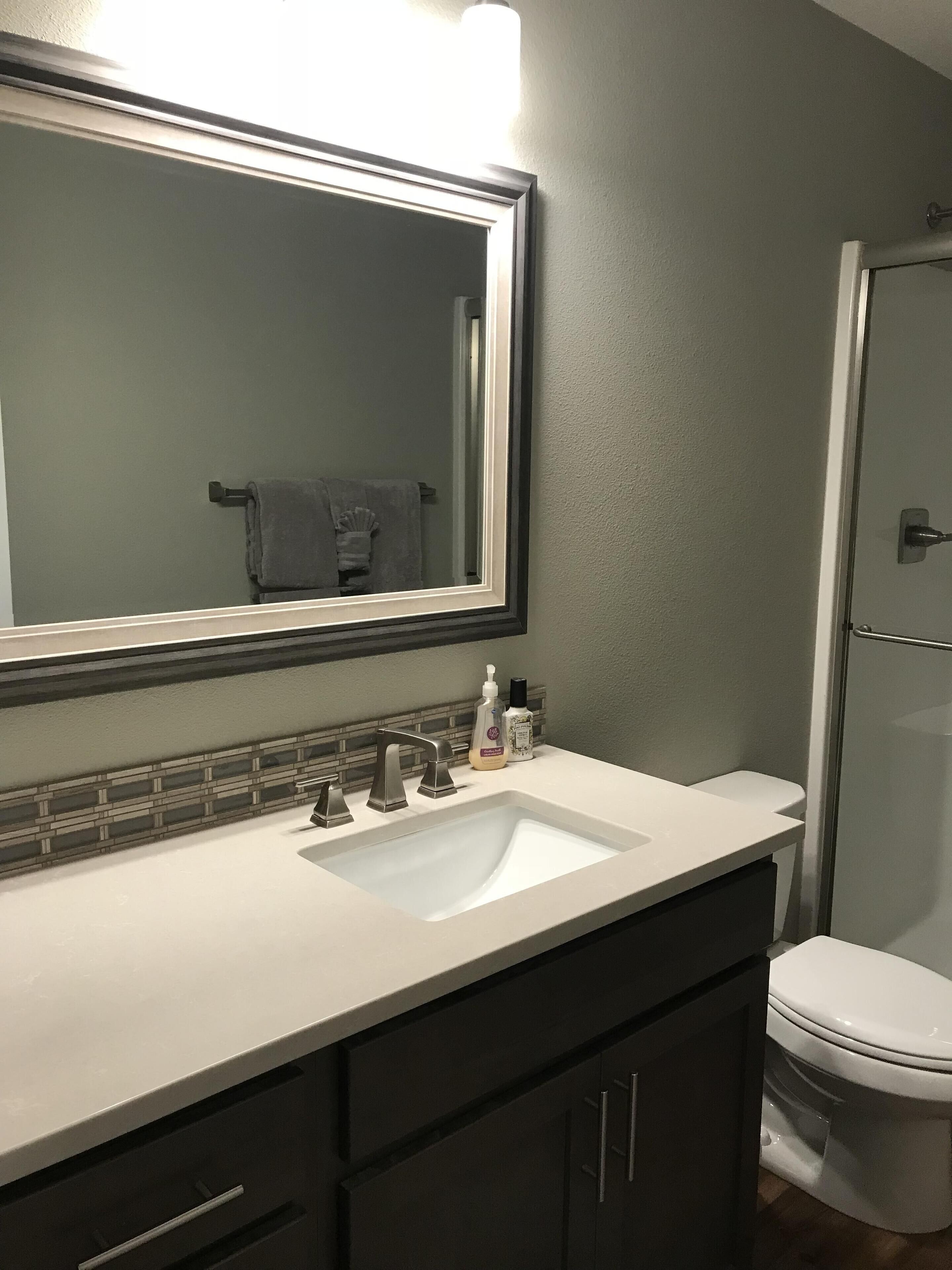 A bathroom with a large mirror, a white sink, dark cabinets, and a toilet.